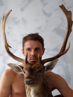 Ross Watson photography of shirtless Jake Shears sitting behind a taxidermy deer head